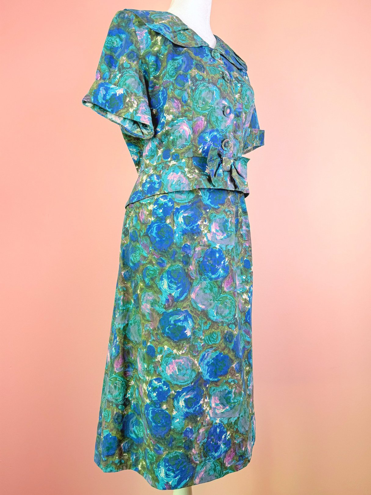 A 1950s women's skirt set in blue with a floral design, featuring a fitted top with a collar and button details, and a matching skirt.