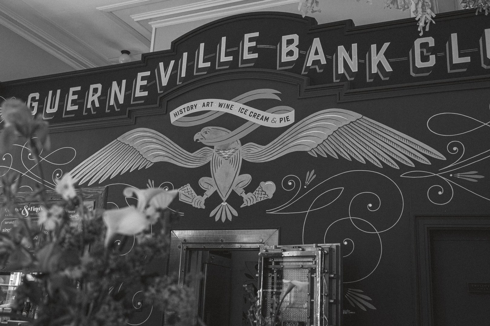 A decorative mural featuring an eagle and the text "Nevi lle Bank" alongside the words "History, Art, Wine, Ice Cream & Pie.