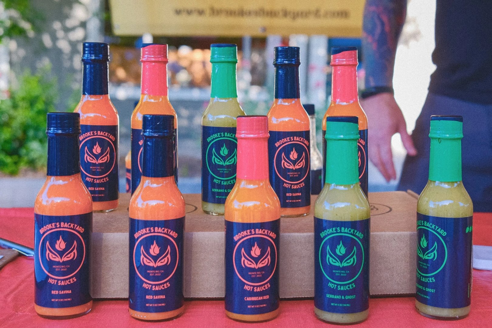 A display of colorful hot sauce bottles with labels featuring a distinctive logo and varying flavors, including Caribbean Red and Red Savina.