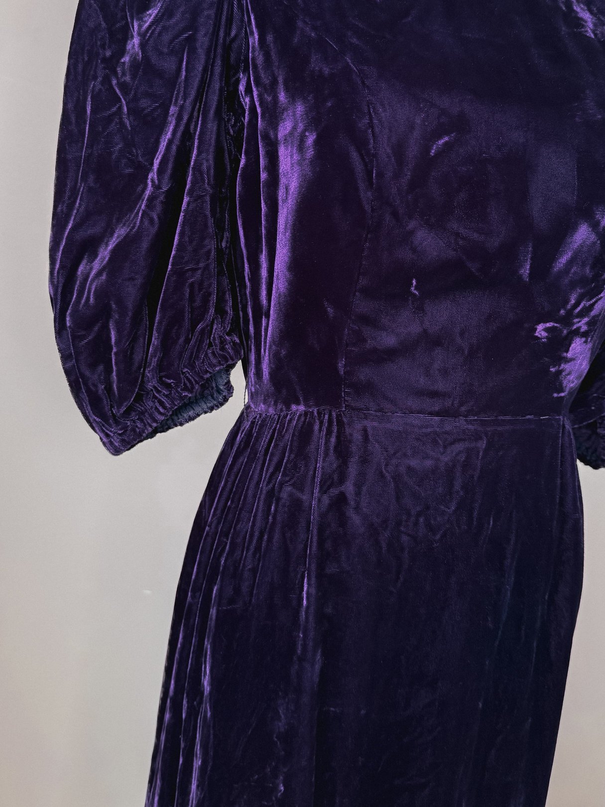 A close-up of a purple velvet dress featuring puffed sleeves and a fitted waist, designed for women in a 1960s style.