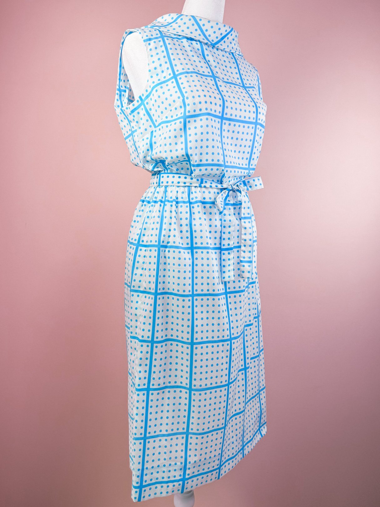 Sleeveless white dress with a blue grid pattern and small circles, featuring a belted waist and a 1970s style.