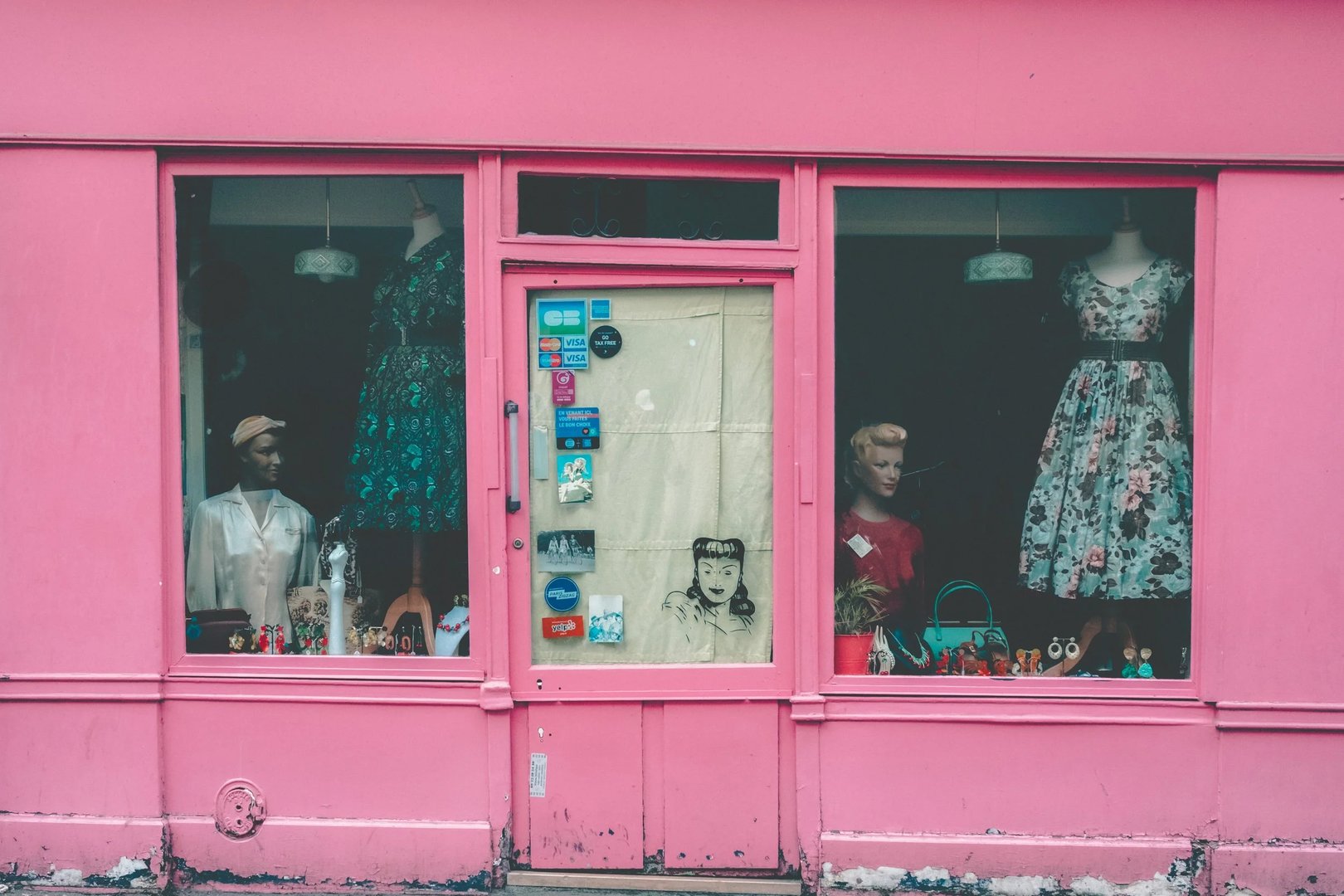 A colorful boutique display featuring mannequins dressed in various vintage-inspired outfits against a pink storefront.