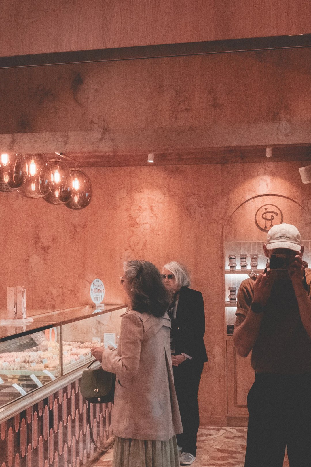 A modern dessert shop interior featuring a display case with colorful pastries and customers browsing in the background.