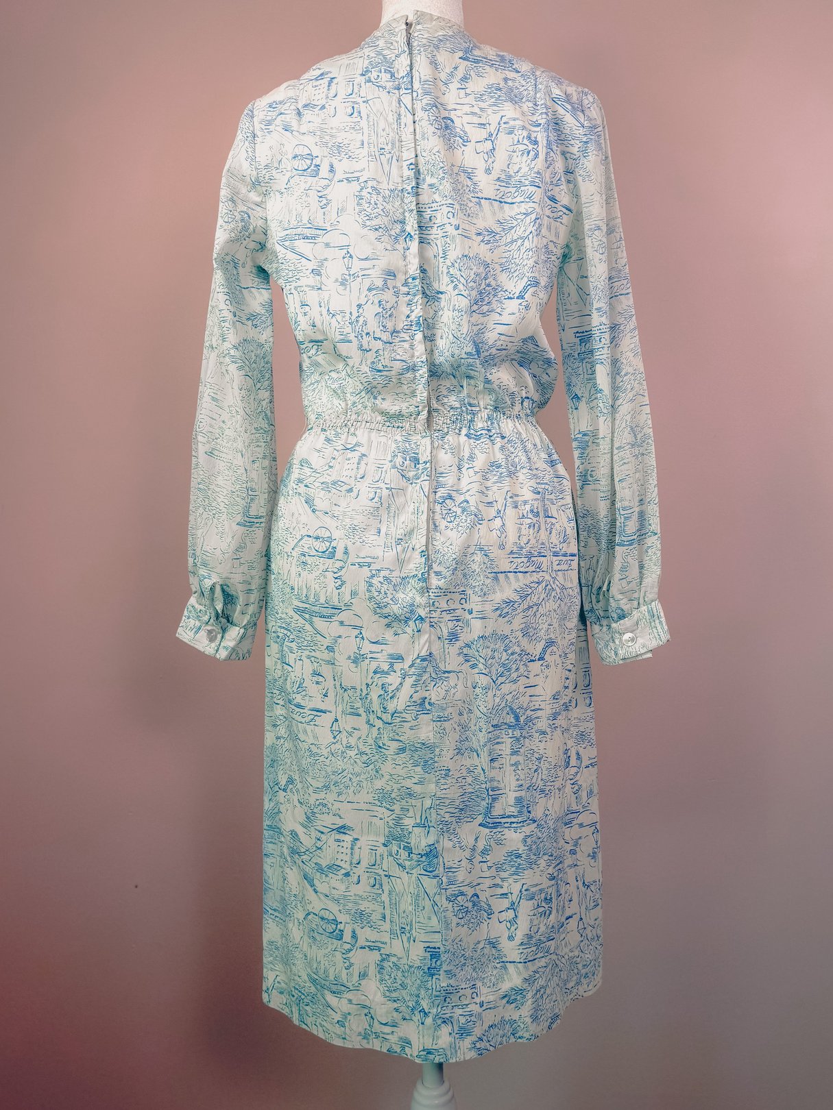 Blue 1960s women's dress featuring a back zipper and gathered waist, with a toile pattern depicting scenic illustrations.