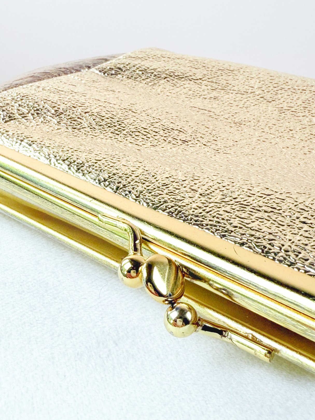 A gold 1950s-style clutch bag with a textured finish and a clasp closure.