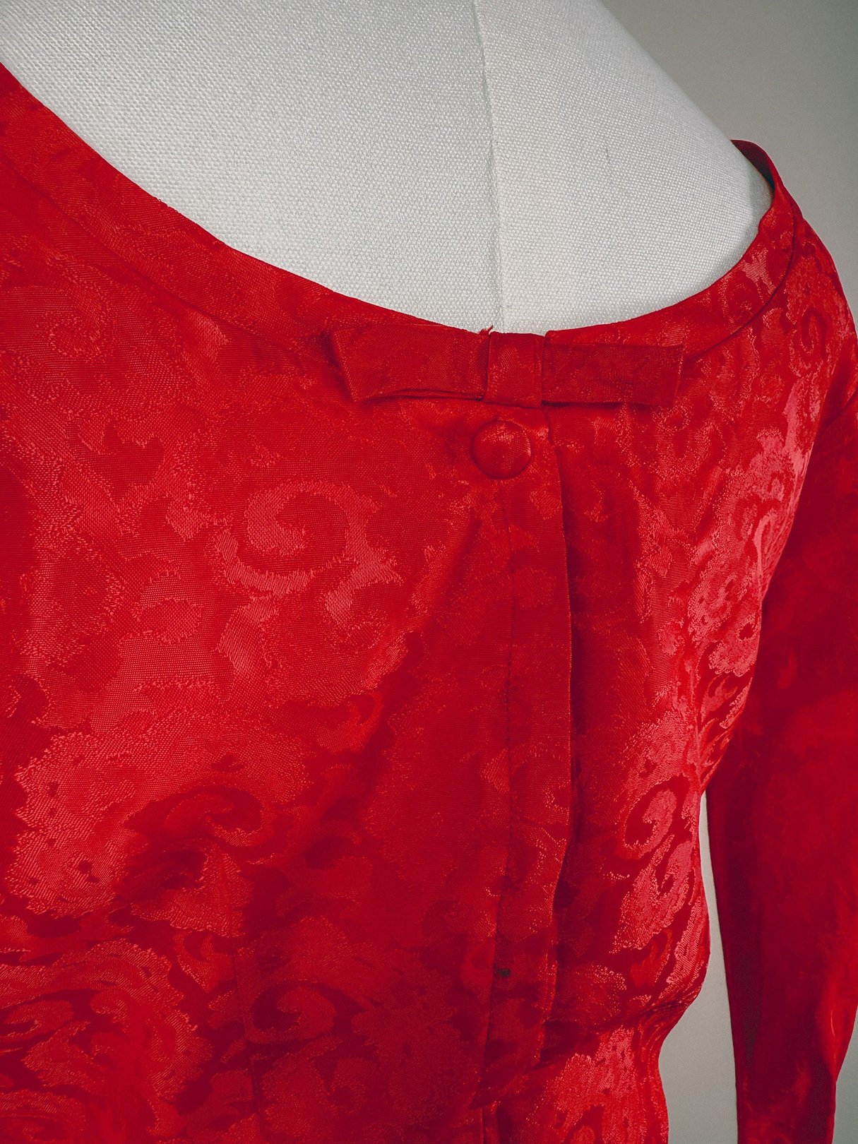 Red damask dress for women from the 1950s featuring a textured pattern and a bow detail at the neckline.