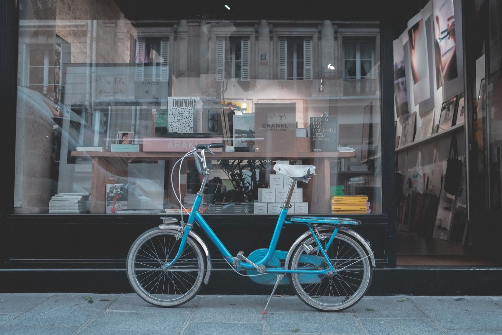 A blue bicycle is parked in front of a bookstore with windows displaying various books and magazines.