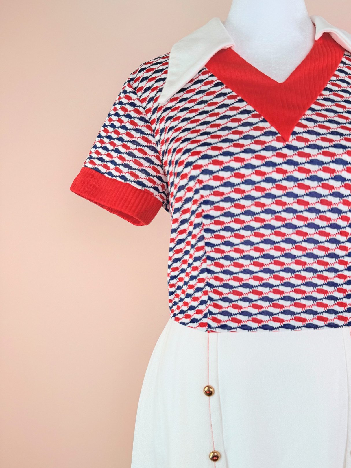 1970s women’s Bottle Rocket Dress featuring a red, white, and blue geometric patterned top with a short sleeve and a white skirt with button details.