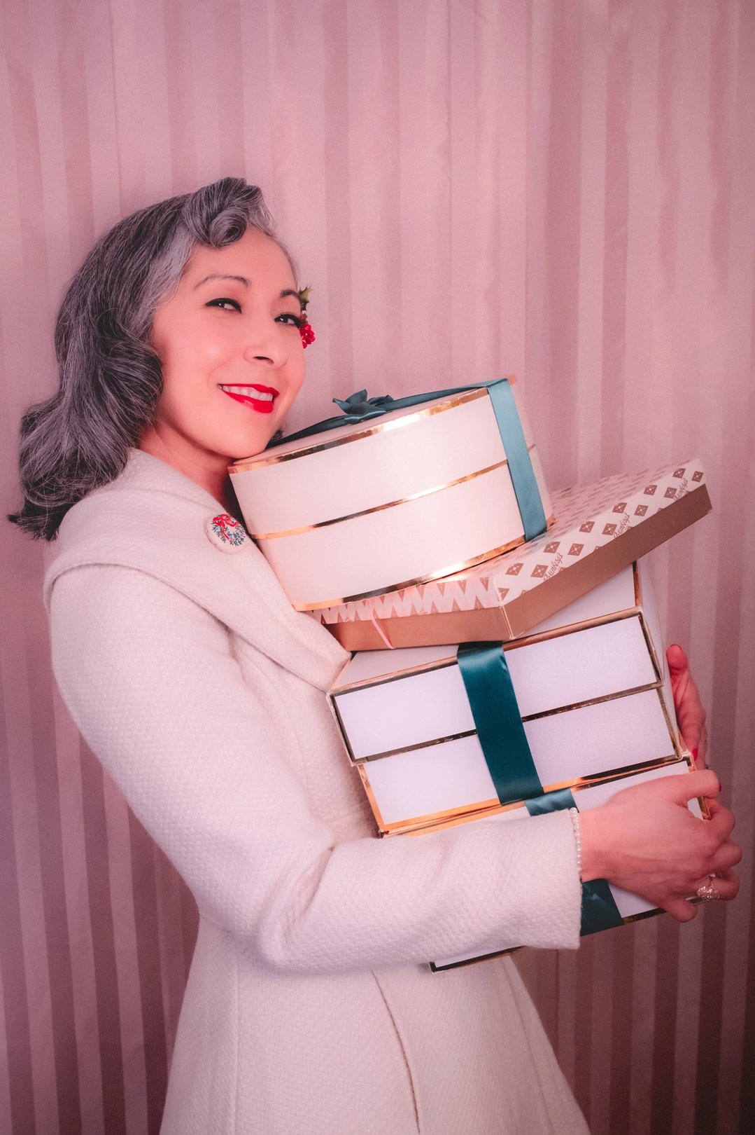 A woman with grey hair smiles while holding several stacked gift boxes.