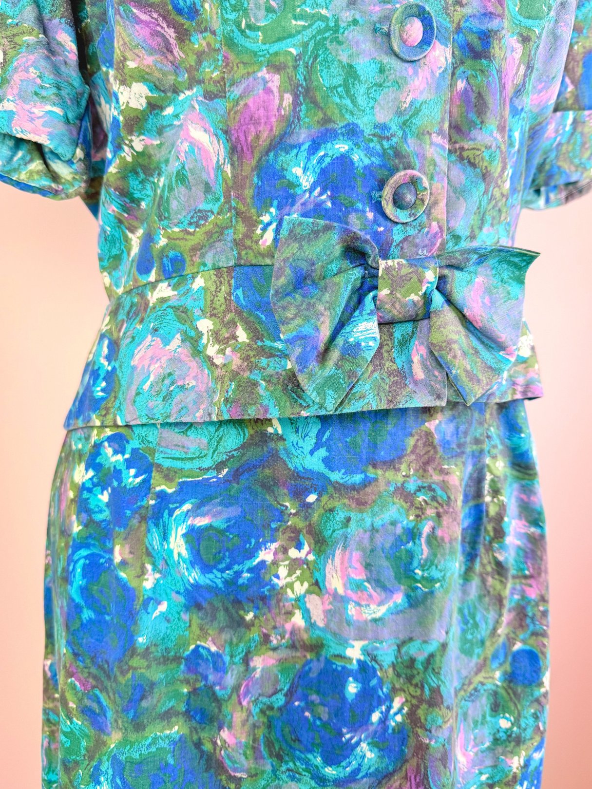 A blue 1950s women’s skirt set featuring a floral pattern, short sleeves, and a bow detail at the waist.