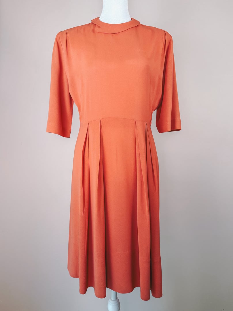 1940s coral Recital dress featuring short sleeves and pleated skirt detail.