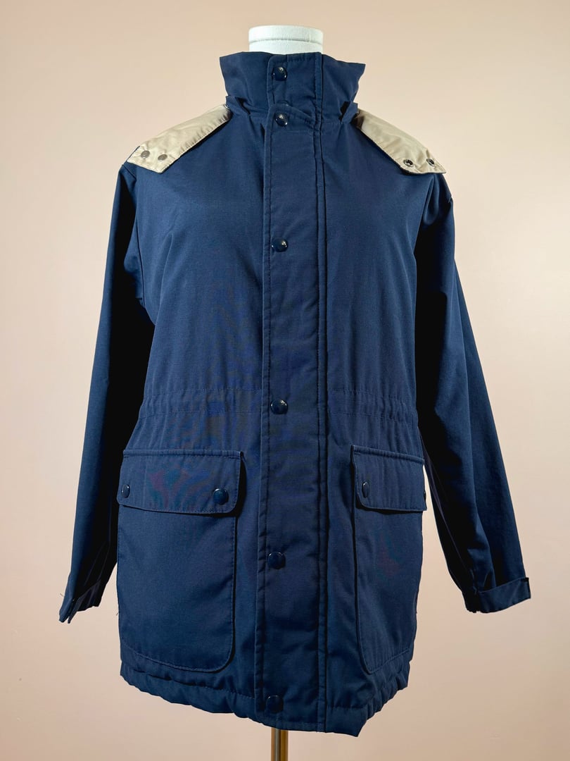 Navy utility field coat for women featuring a zip and snap front closure, two front pockets, and beige shoulder patches, inspired by 1970s design.