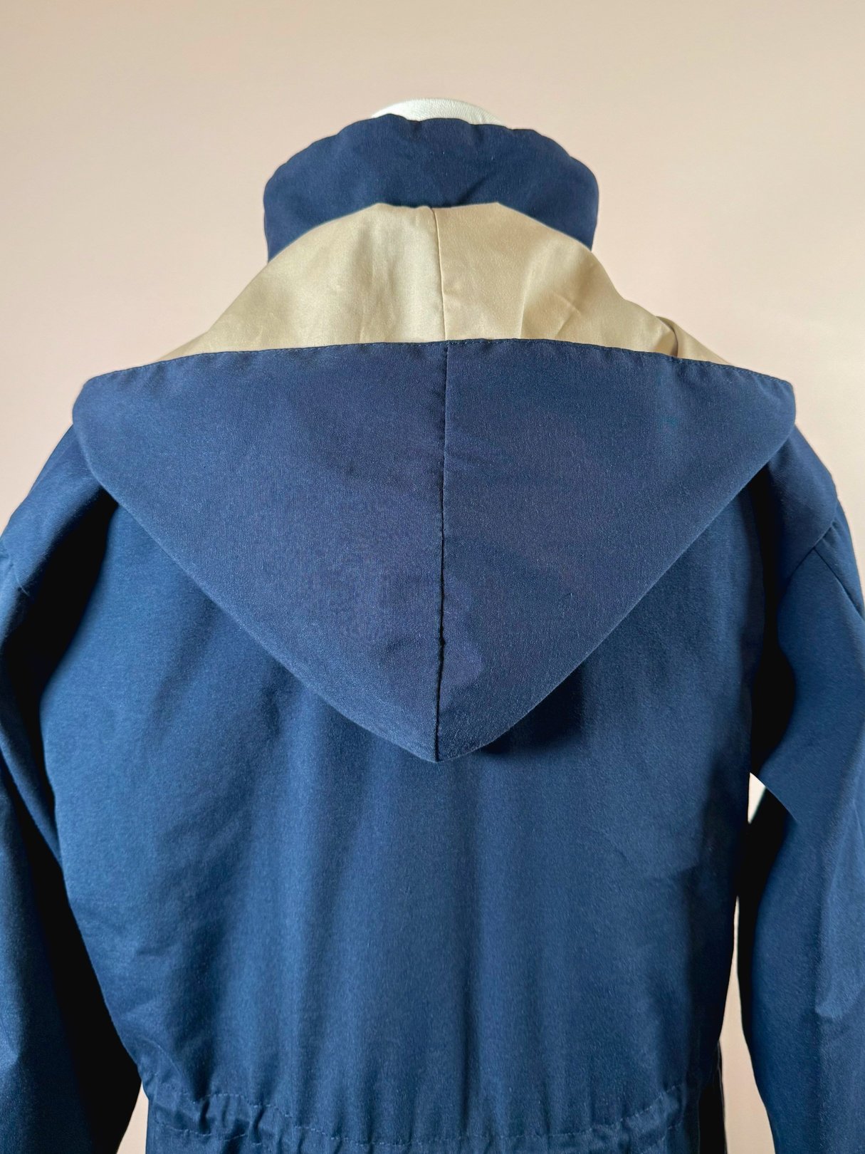 Navy blue women's utility field coat from the 1970s featuring a tan hood and a cinched waist.