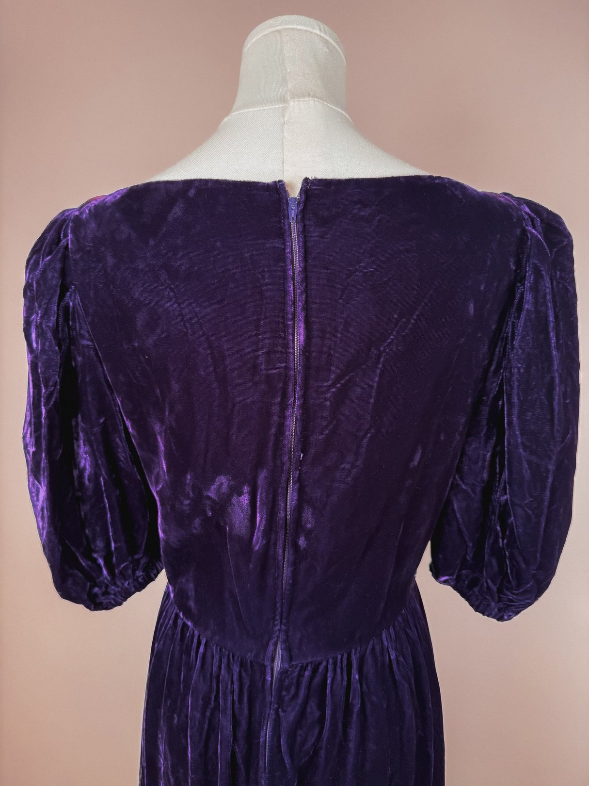 A 1960s women's dress in purple velvet featuring puffed sleeves and a zipper closure at the back.