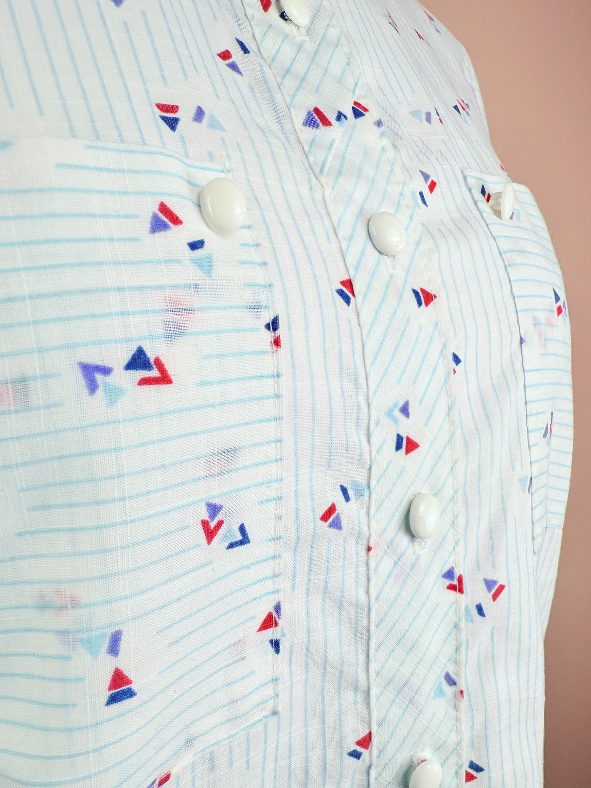 Blue 1980s women's top with a pattern of red and blue triangles and vertical stripes, featuring front buttons and pockets.