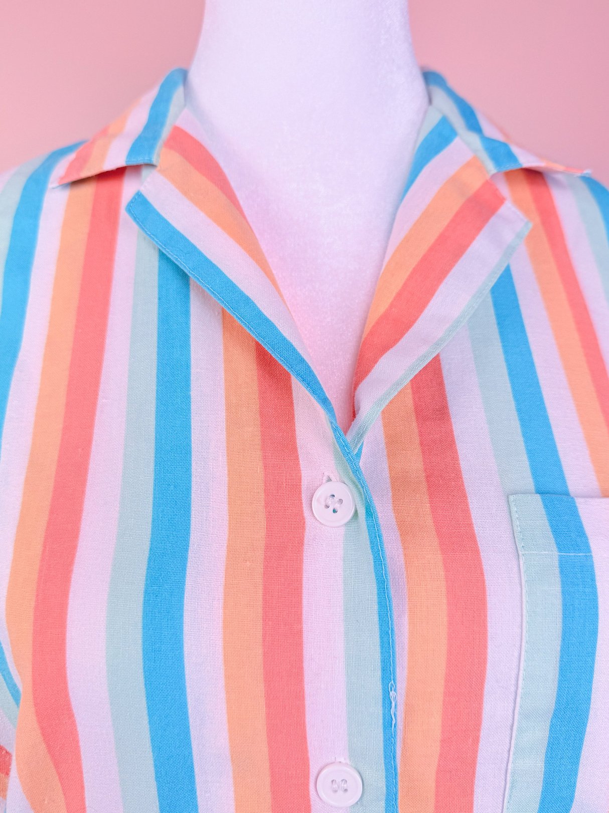 Colorful striped romper featuring blue, peach, and mint hues with a classic collar and button-up front.