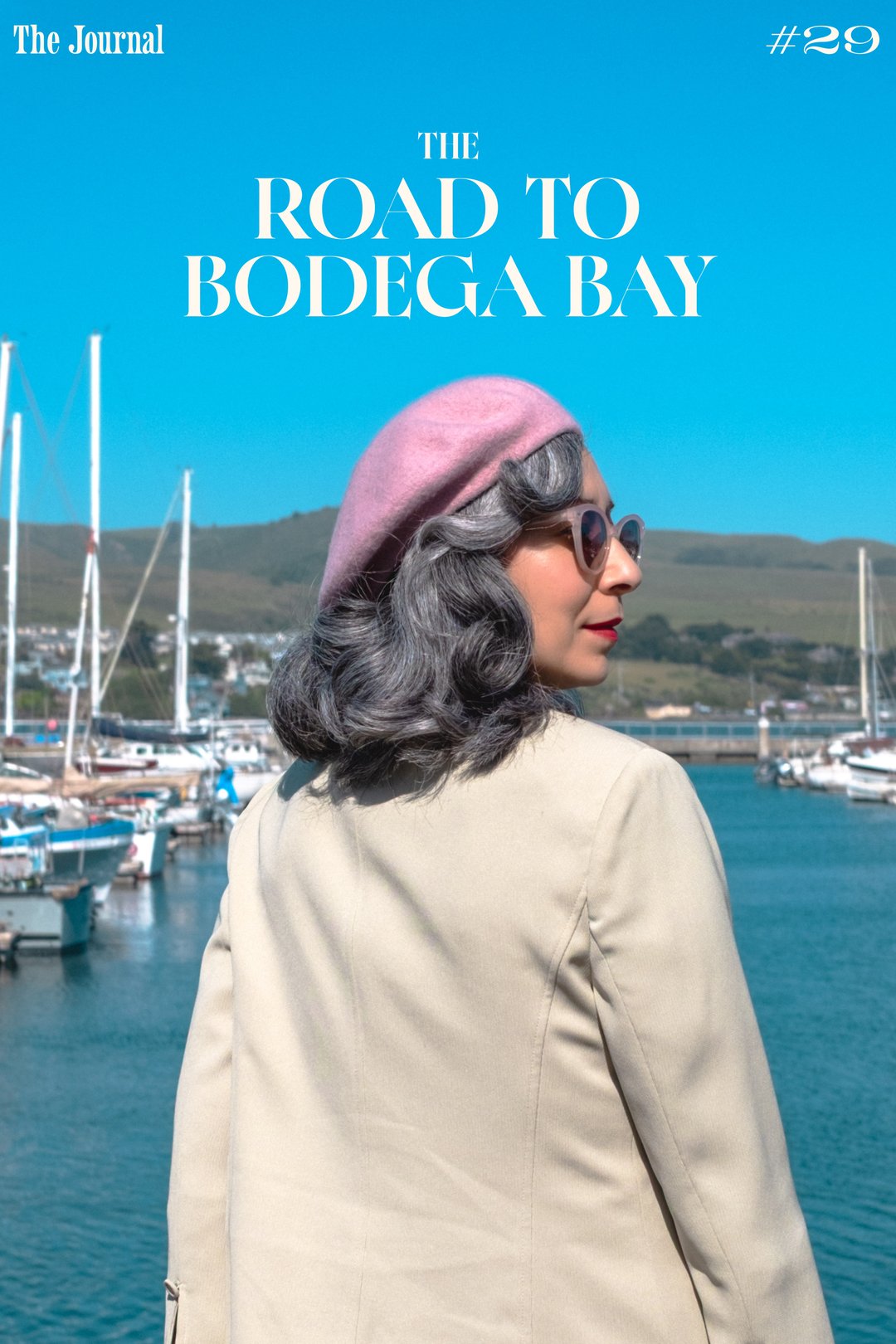 The Road to Bodega Bay: A woman with gray hair and a pink beret stands by a marina filled with boats, with green hills in the background and the title "The Road to Bodega Bay" prominently displayed above