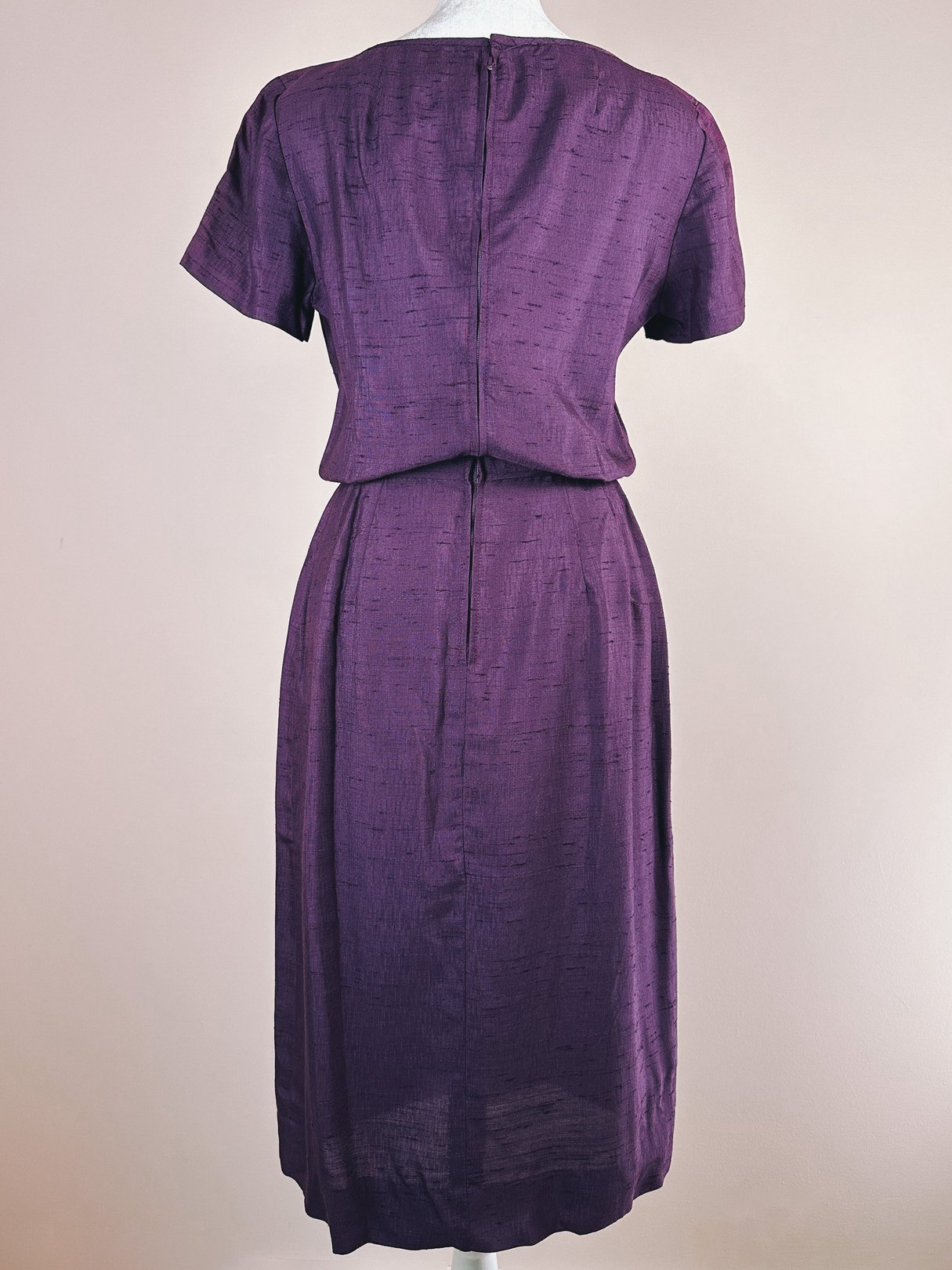 Back view of a 1960s women's purple dress featuring a bow detail and a fitted silhouette.