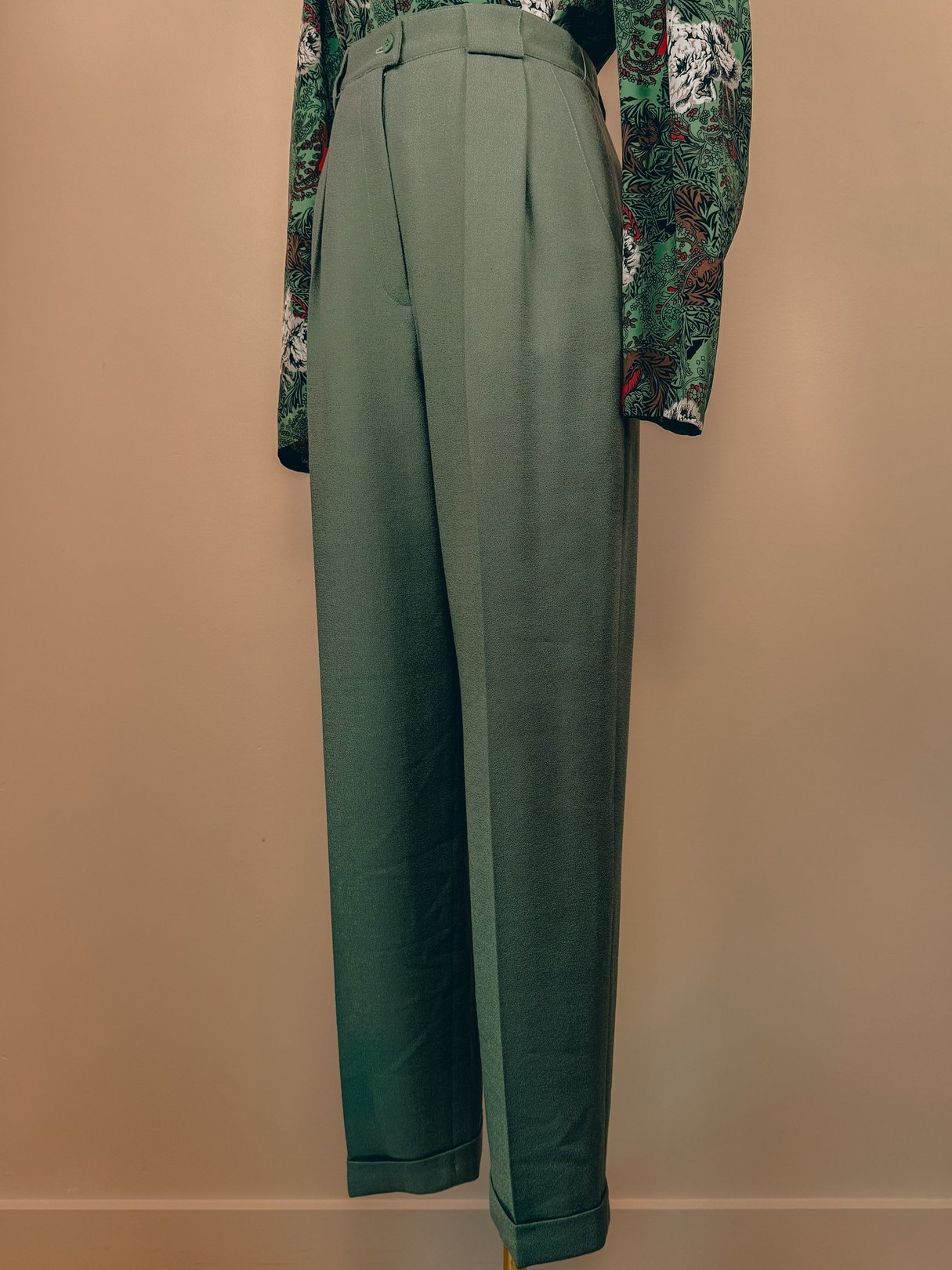 Sage green pleated trousers for women, designed in a loose fit, showcasing a high waist and a wide leg style typical of the 1980s.