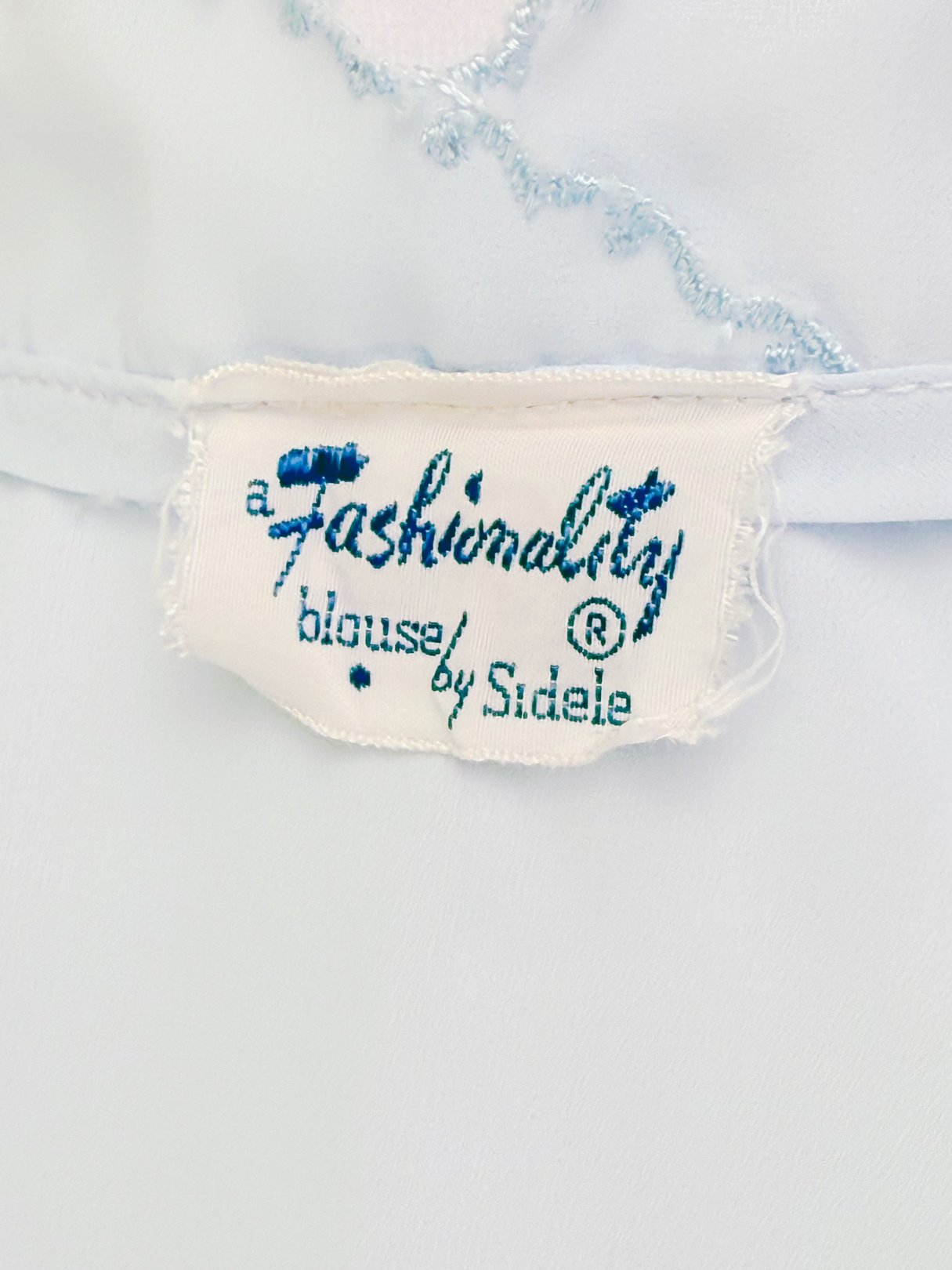 Powder blue blouse with a tag reading "a Fashionably blouse by Sidele.