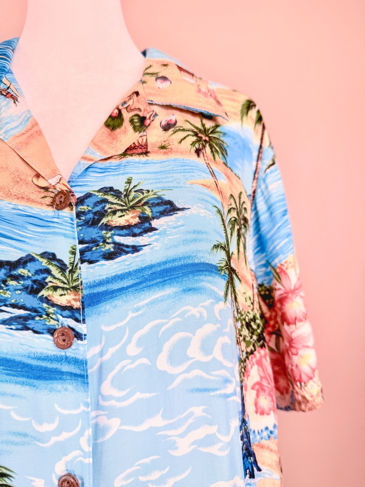 Blue 1960s women's tropical print top featuring palm trees and beach scenes with a button-up front.