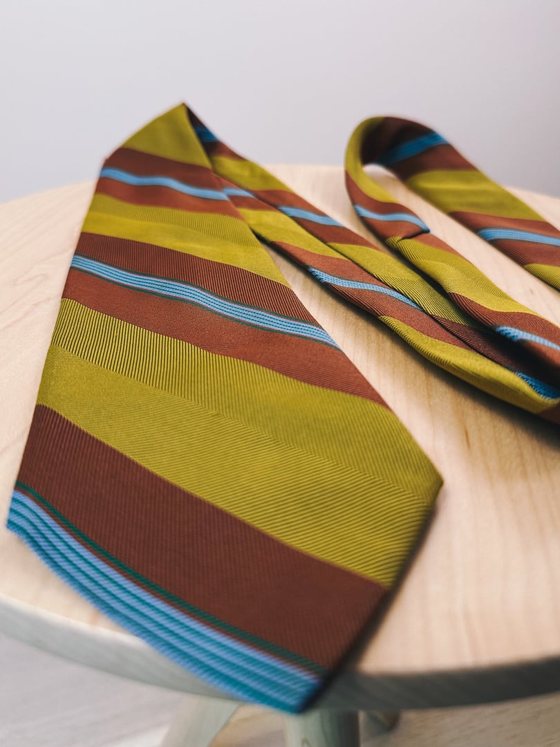 Chartreuse tie with horizontal stripes in brown and blue, styled for women's fashion from the 1970s, displayed on a wooden surface.