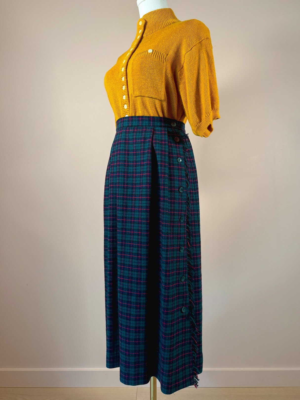 A green plaid skirt from the 1970s, featuring large buttons and a side button closure, paired with a mustard yellow top.