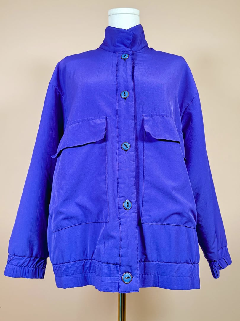 Vibrant violet 1980s women's jacket featuring a high collar, two front pockets, and button closures.