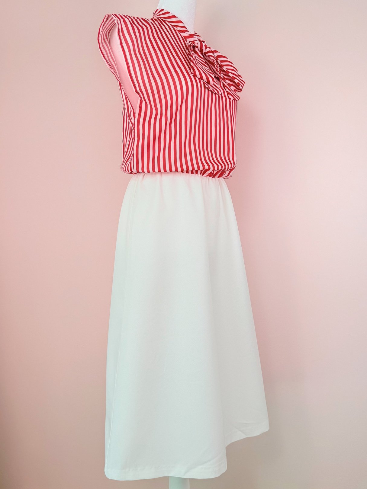 Red and white candy stripe dress with a bow at the neckline, featuring a fitted top and a flowing white skirt, inspired by 1970s fashion.