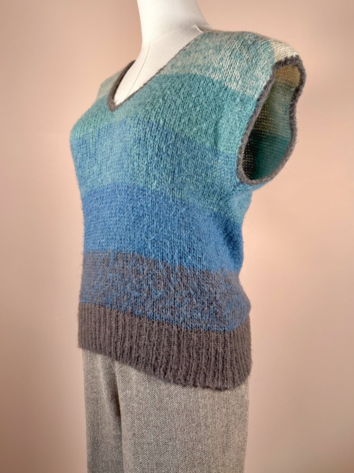 Lightweight blue mohair sweater vest with a V-neck and a color-blocked design, featuring shades of teal and gray, styled for women in a 1970s fashion.
