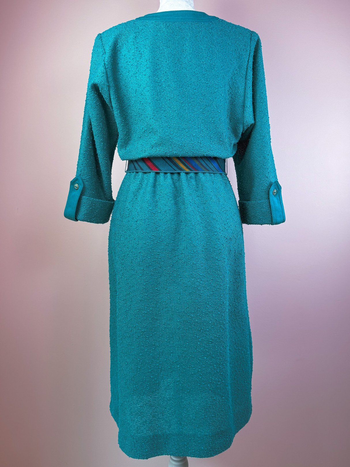 Teal 1980s dress featuring a textured fabric and a multi-striped belt at the waist.