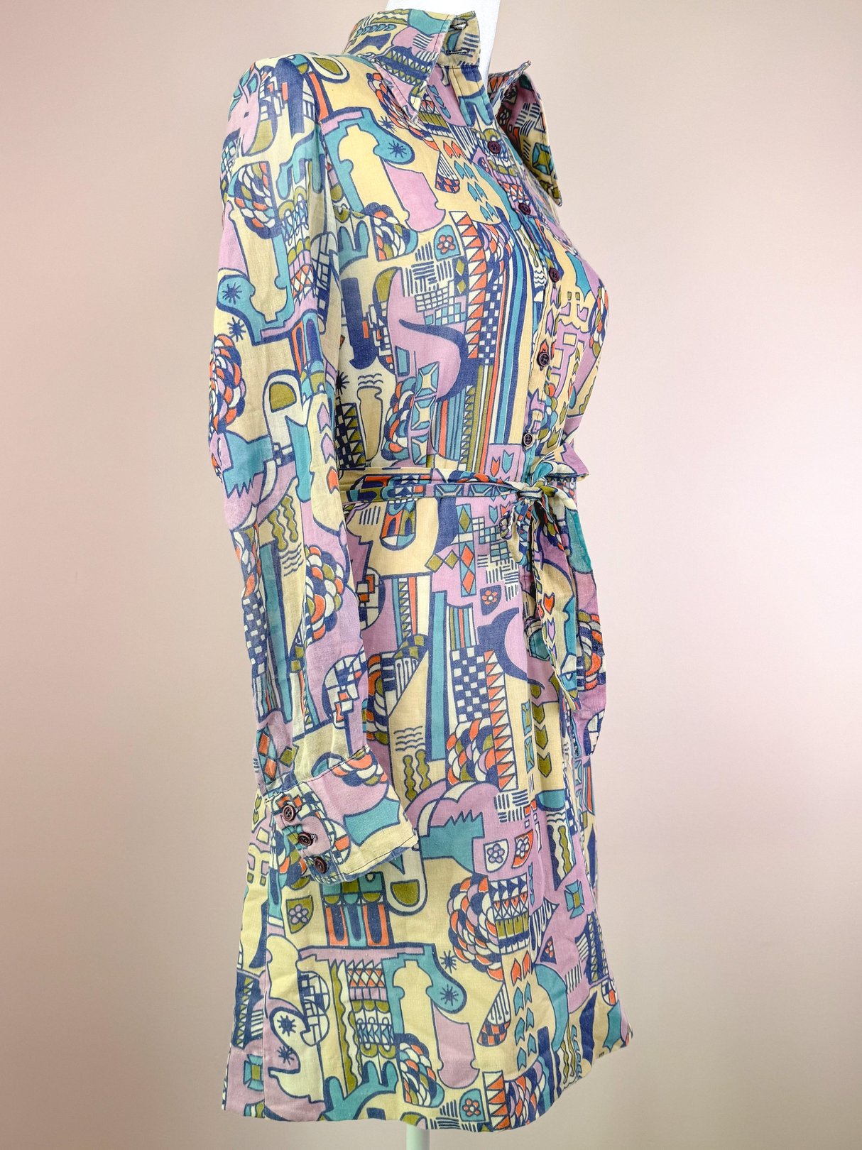 Cream 1970s Metropolis Dress featuring a colorful abstract pattern, long sleeves, and a tie belt at the waist.
