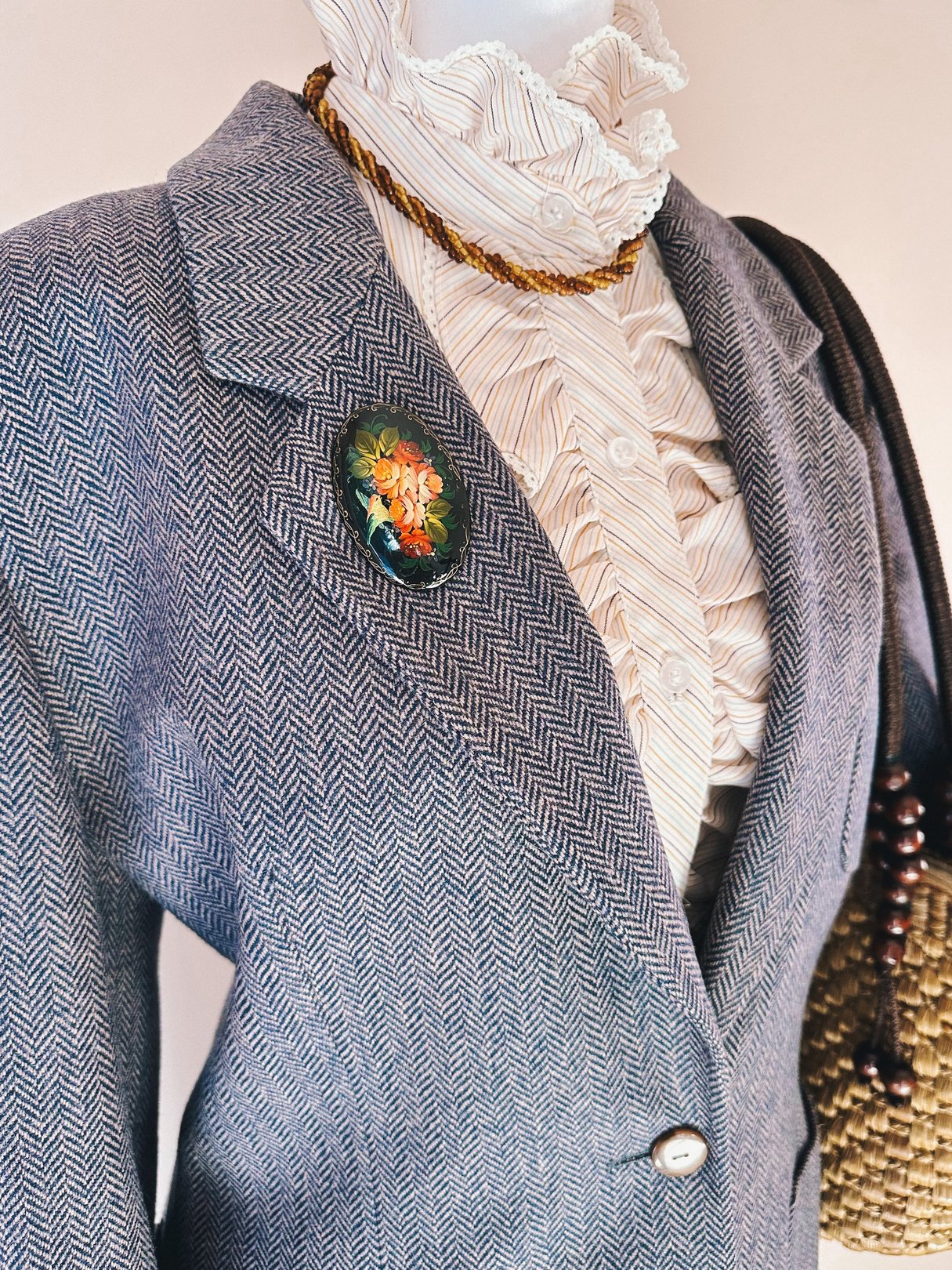 A black 1970s Fluttering Bird Brooch featuring floral designs is attached to a herringbone-patterned blazer on a mannequin.