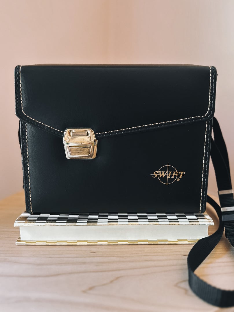A black 1970s camera bag from Swift Adventure Club with a gold clasp and a checkered base.