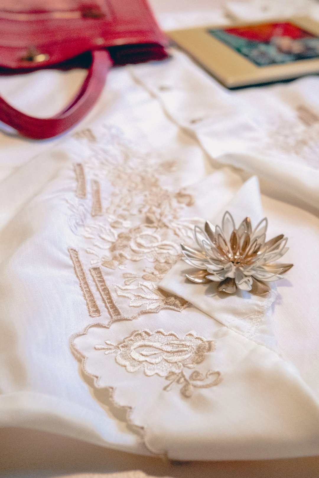 A close-up of white fabric featuring intricate embroidery and a decorative lotus flower brooch.