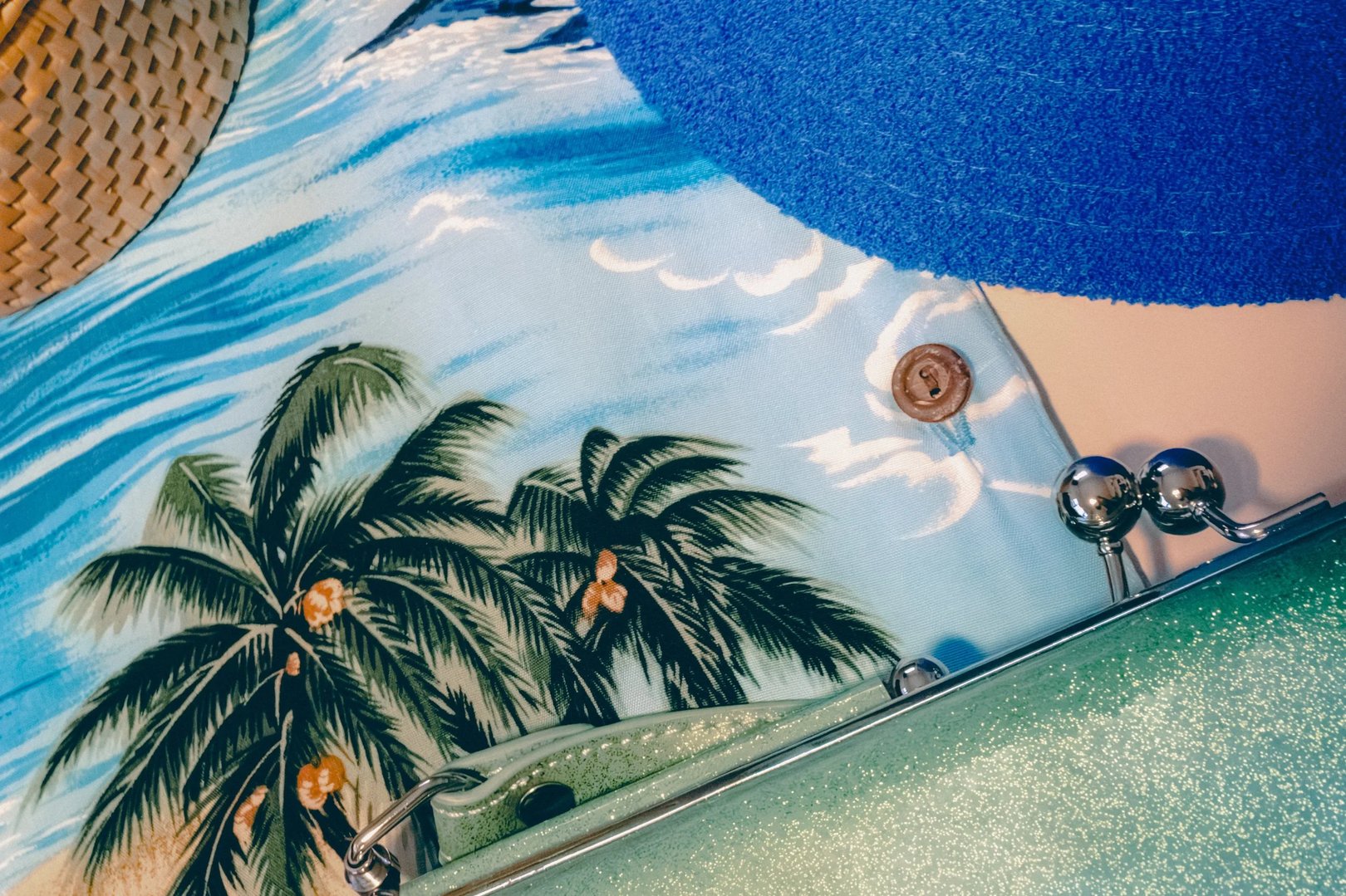 A colorful beach-themed arrangement featuring a palm tree print fabric, a blue sun hat, and a metallic clutch.
