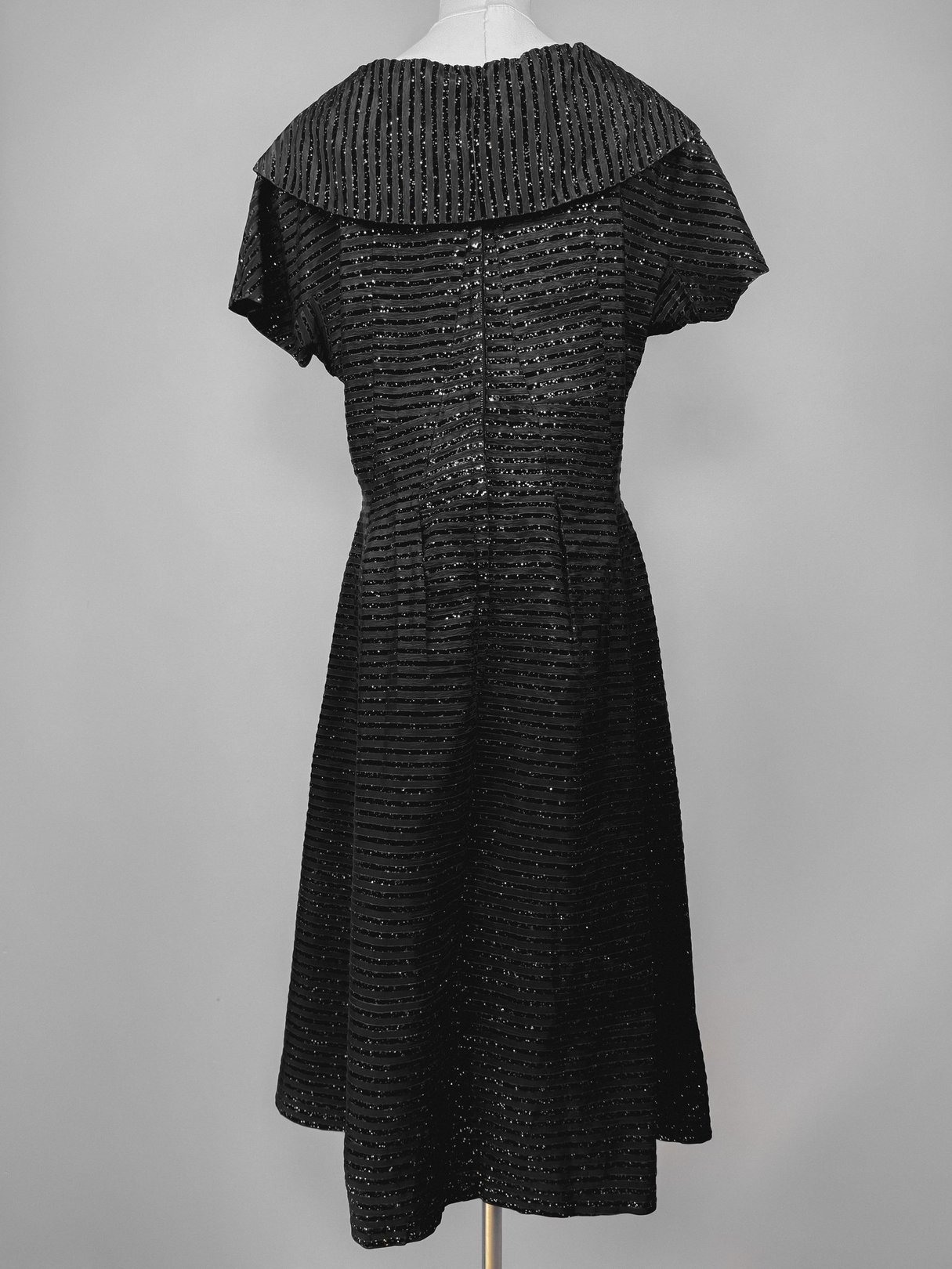 Black 1950s women's confetti party dress featuring a textured fabric and a wide collar, displayed from the back.