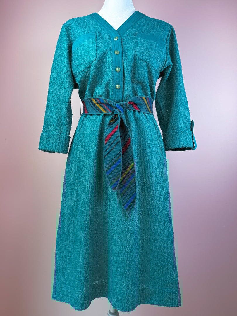 Teal 1980s dress featuring a button-up front, two chest pockets, and a multicolored striped belt.