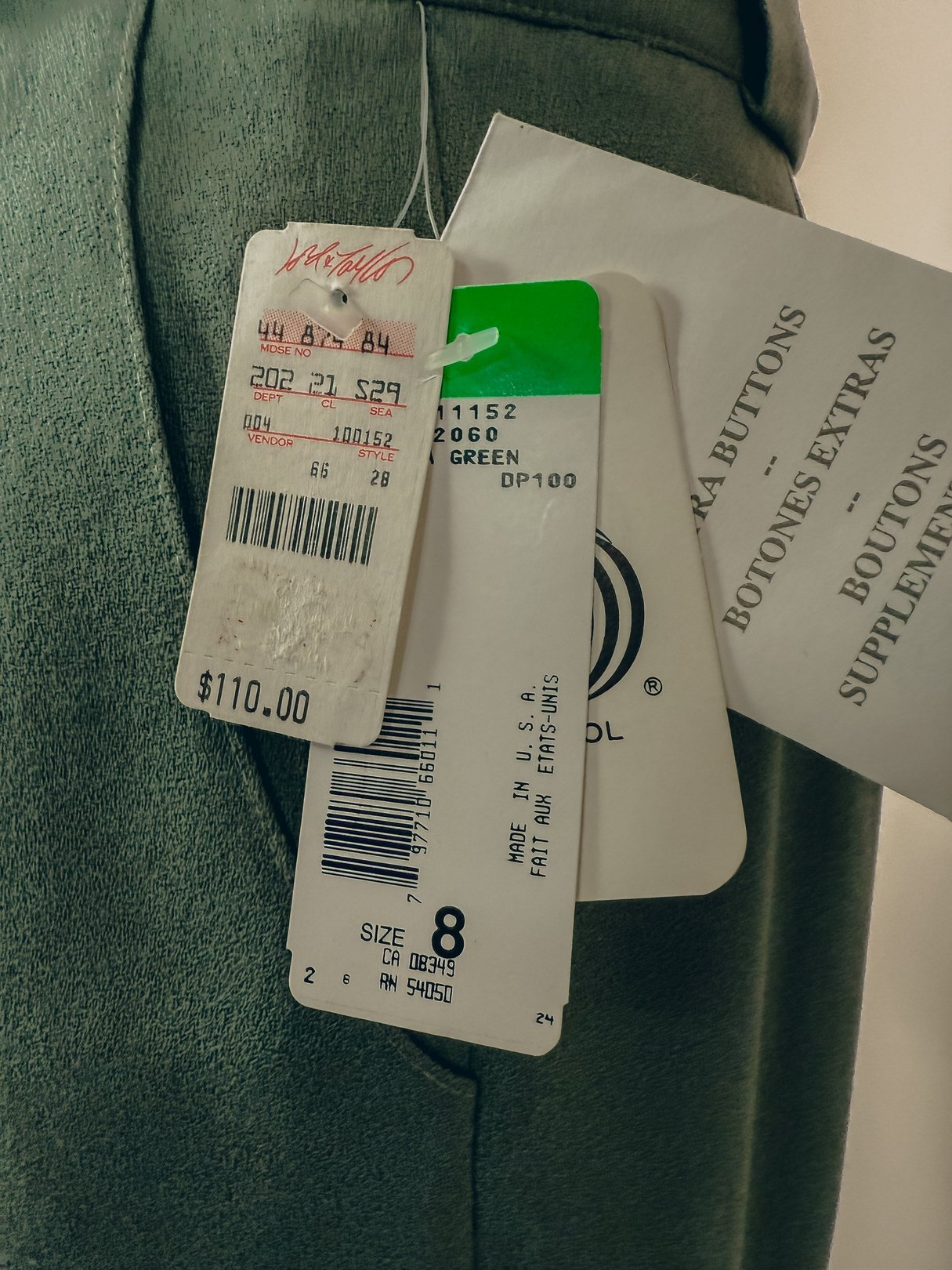 Sage green pleated trousers for women from the 1980s, size 8, with multiple tags showing a price of $110.00.