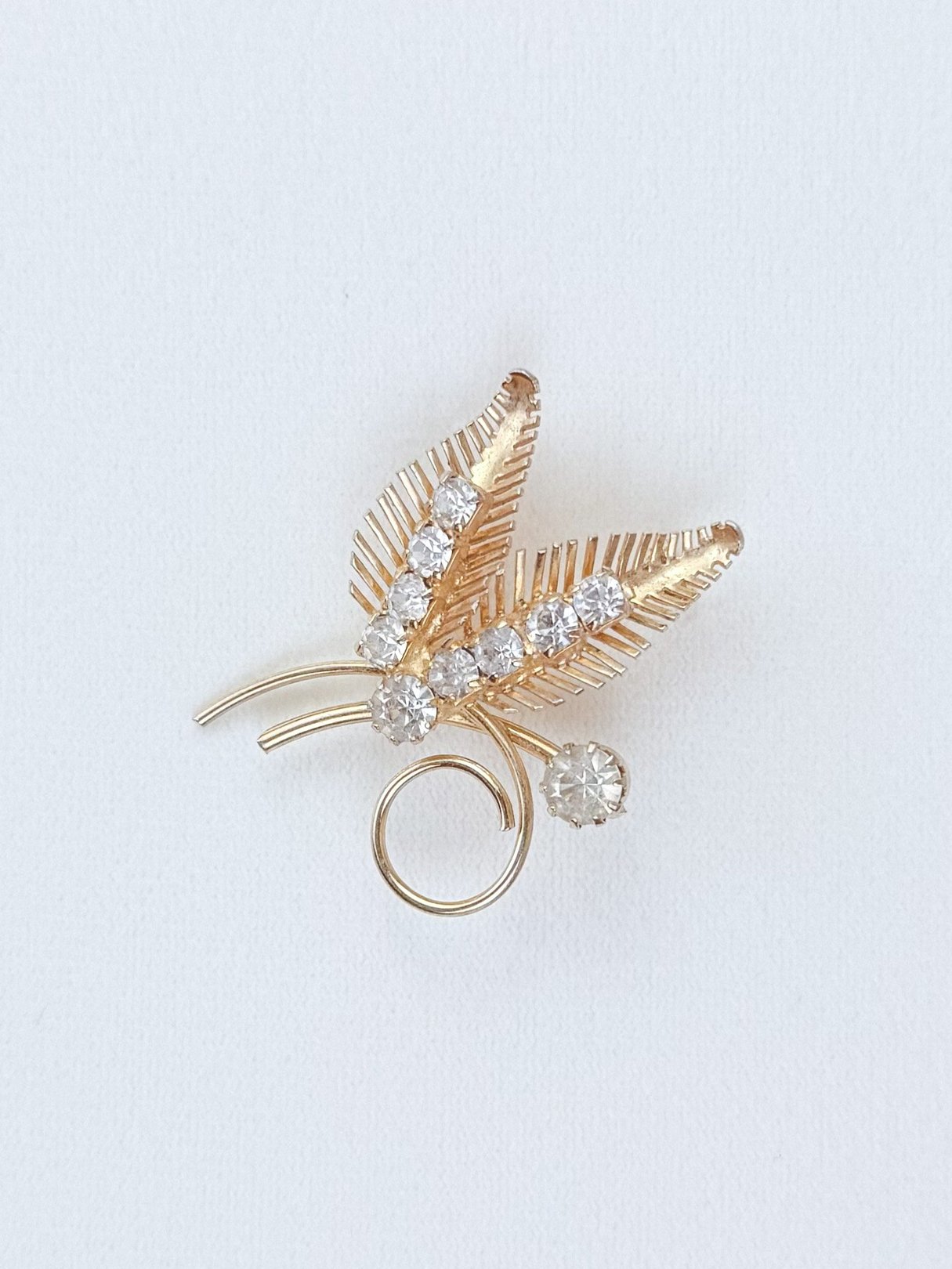 Gold tone brooch featuring a fern design adorned with clear rhinestones, dating from the 1950s, suitable for women's accessories.