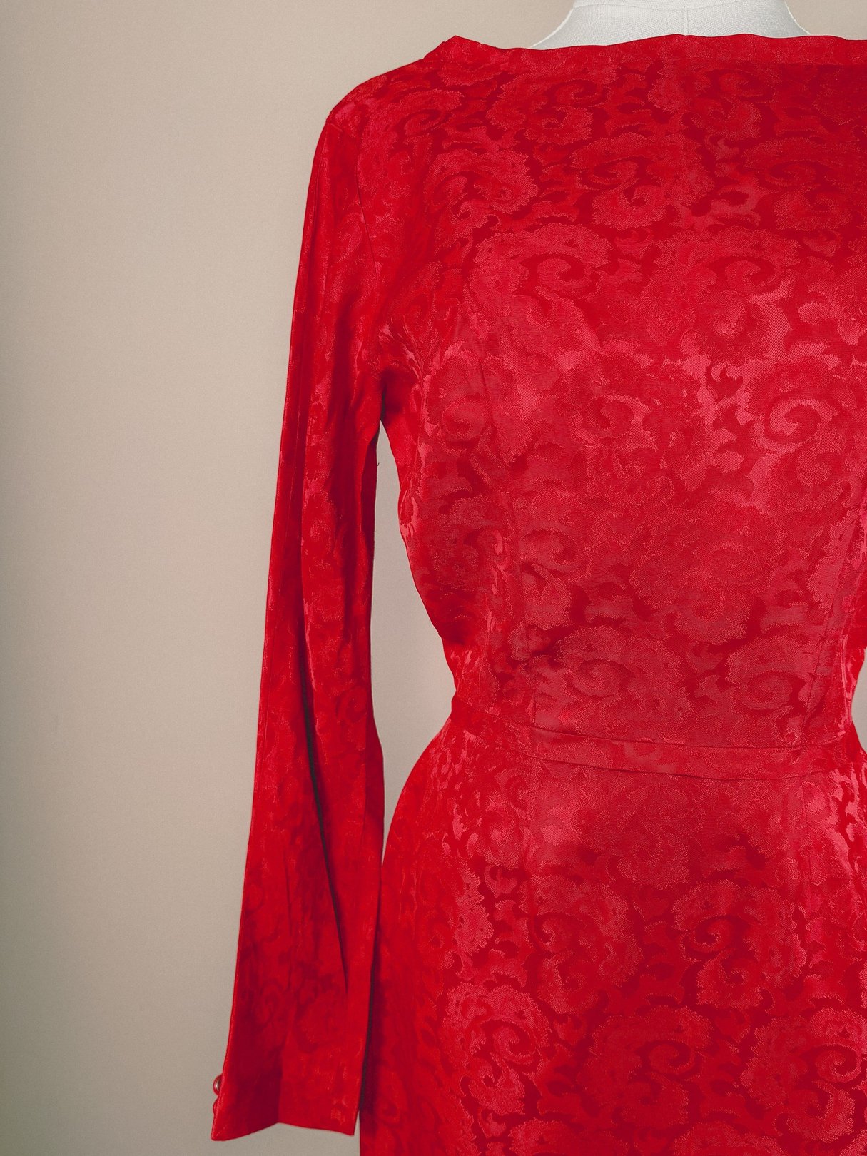 A red damask dress for women from the 1950s featuring long sleeves and a textured fabric.