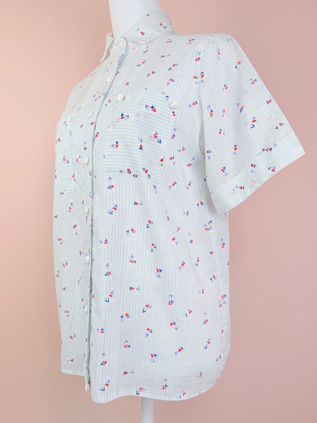 Blue 1980s women's short-sleeve top featuring a white base with a colorful geometric print and two chest pockets.