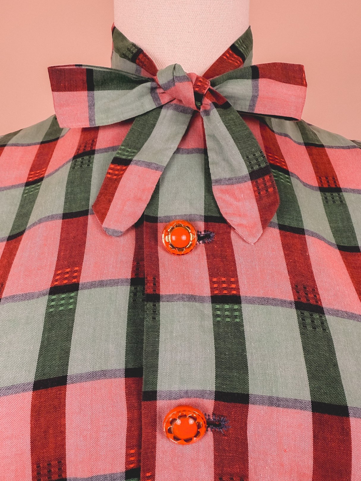 Red and green plaid dress with a bow tie collar and button details, reflecting 1950s women's fashion.