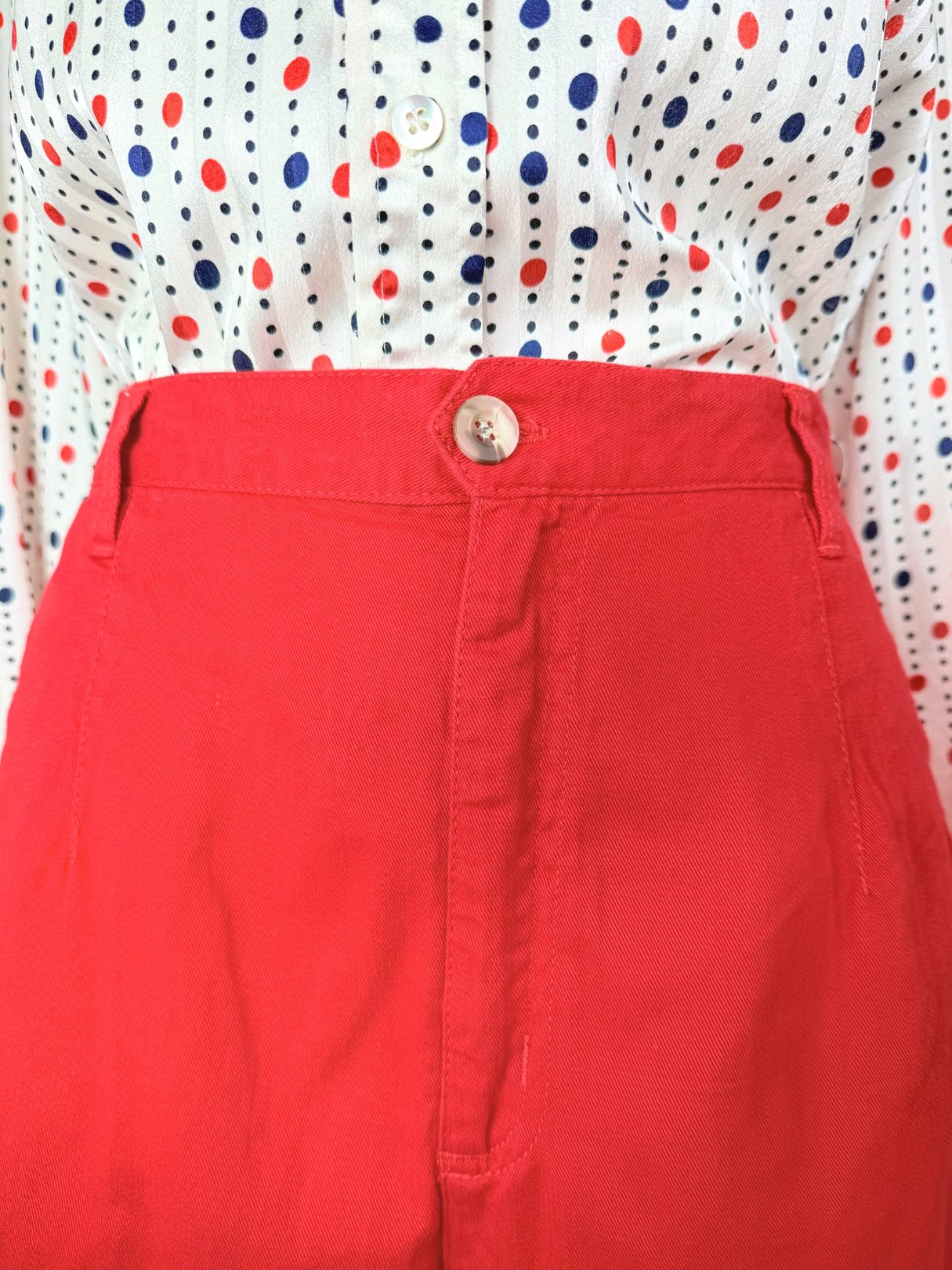 High-waisted red shorts featuring a button closure, styled with a polka-dotted blouse.