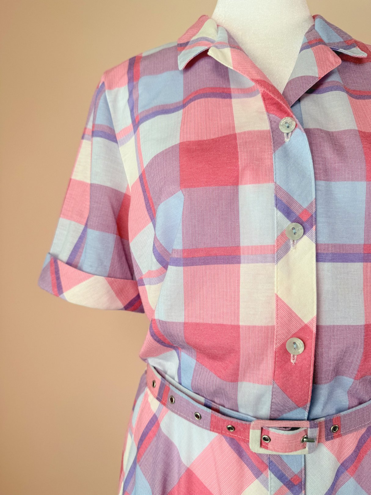 1950s women's purple picnic plaid dress featuring a button-up front, short sleeves, and a belted waist with a multicolored check pattern in pink and blue.