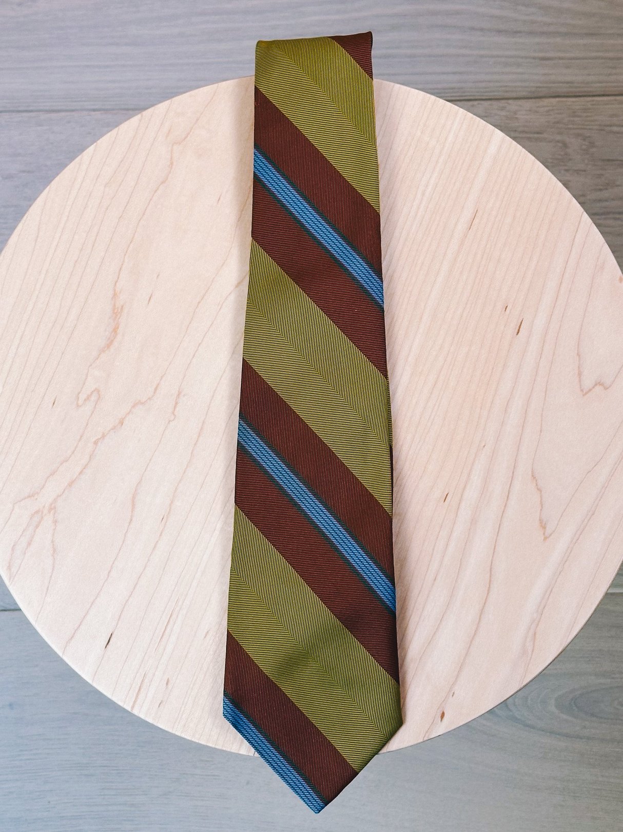 A women's 1970s tie in chartreuse with diagonal stripes of brown and blue, displayed on a round wooden surface.