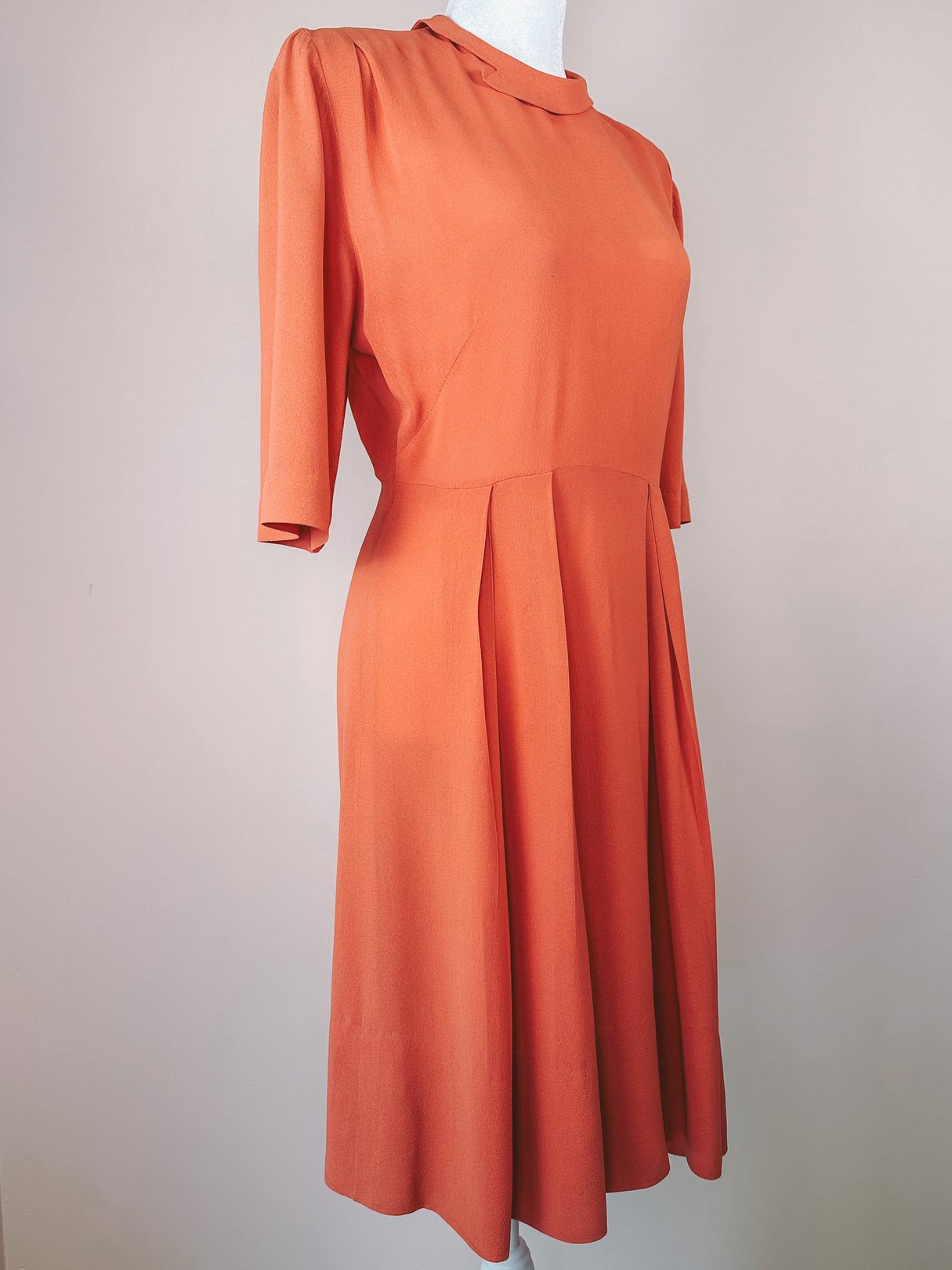 1940s coral dress featuring a rounded neckline, short sleeves, and a pleated skirt.