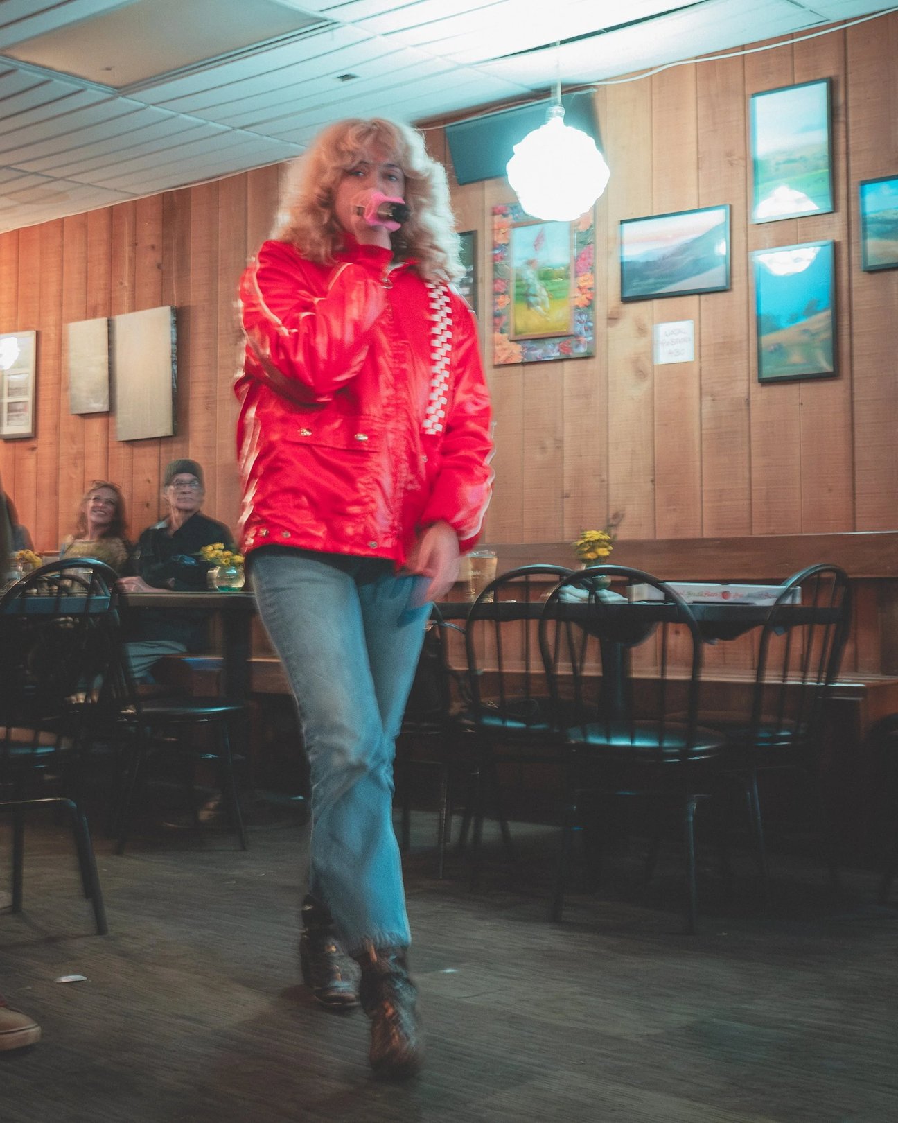 A person in a red jacket with a checkered pattern walks through a cafe with wooden walls and framed pictures.