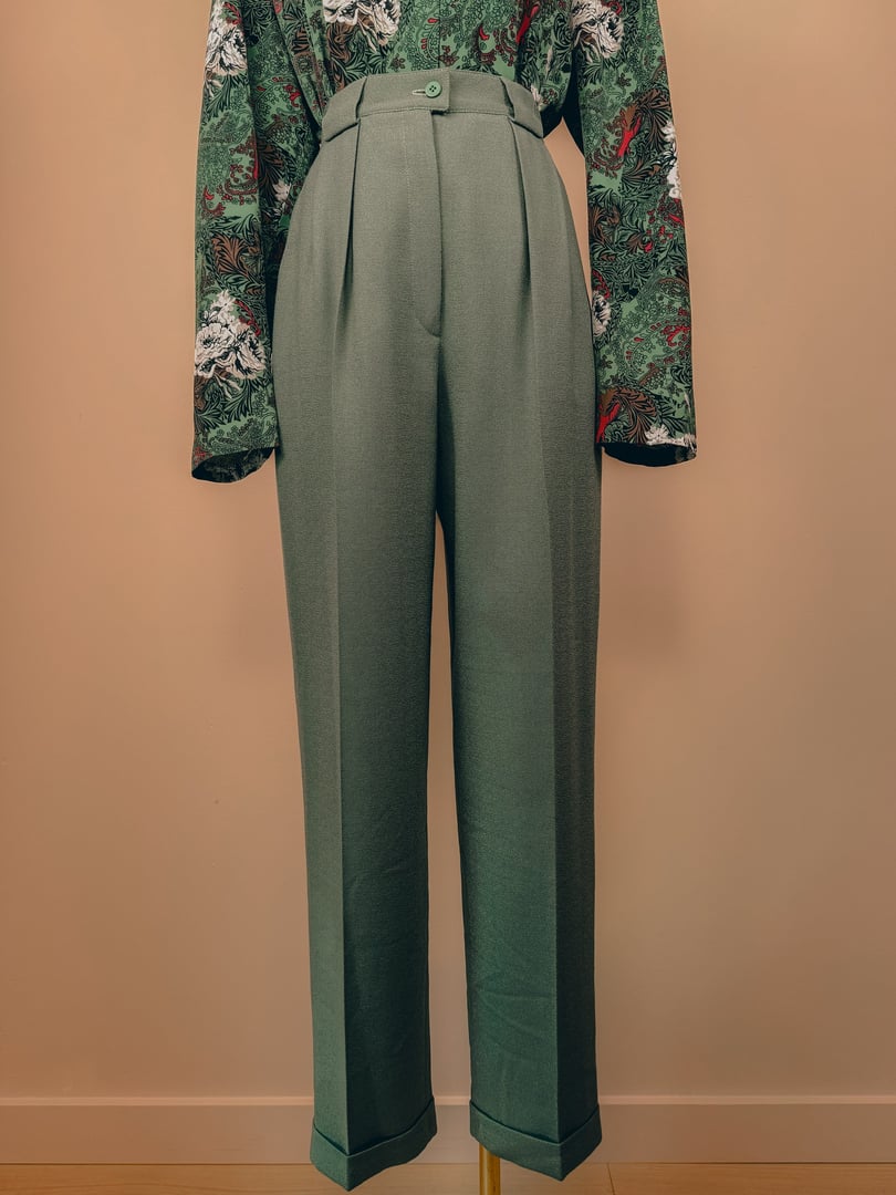 Sage green pleated trousers for women, featuring a high waist and tailored fit, styled in a 1980s fashion.