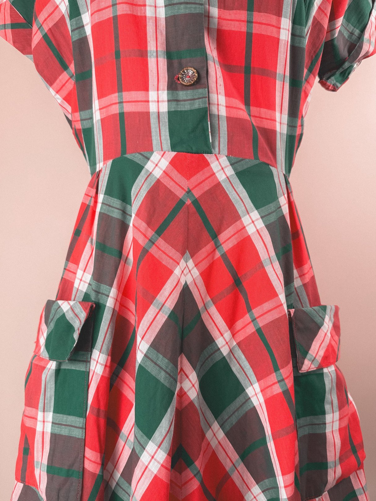 Red and green plaid dress with short sleeves, a button closure, and two front pockets, characteristic of 1950s women's fashion.